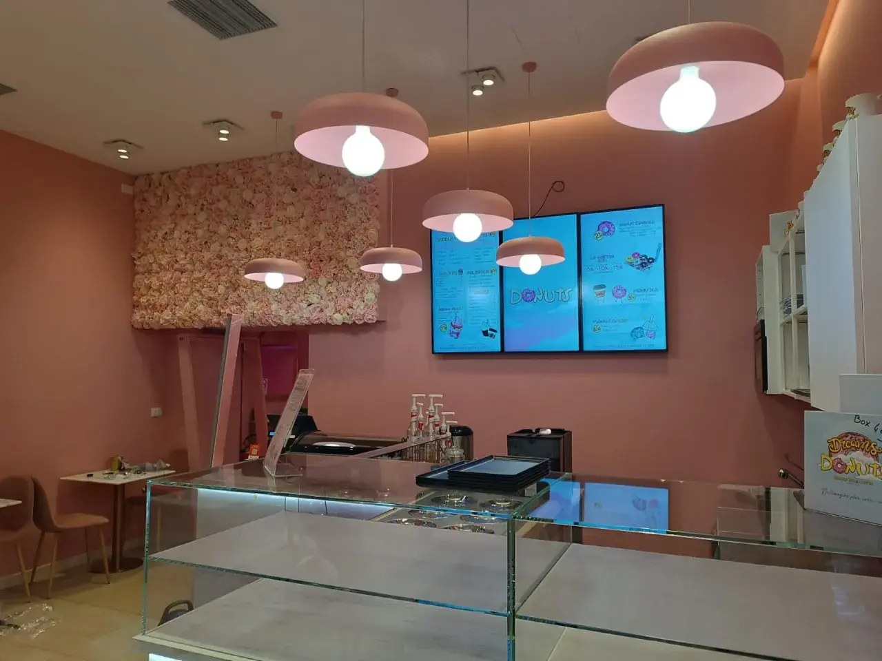 Cinq luminaires identiques, de couleur rose, éclairent un salon de thé aux murs ornés de fleurs roses.