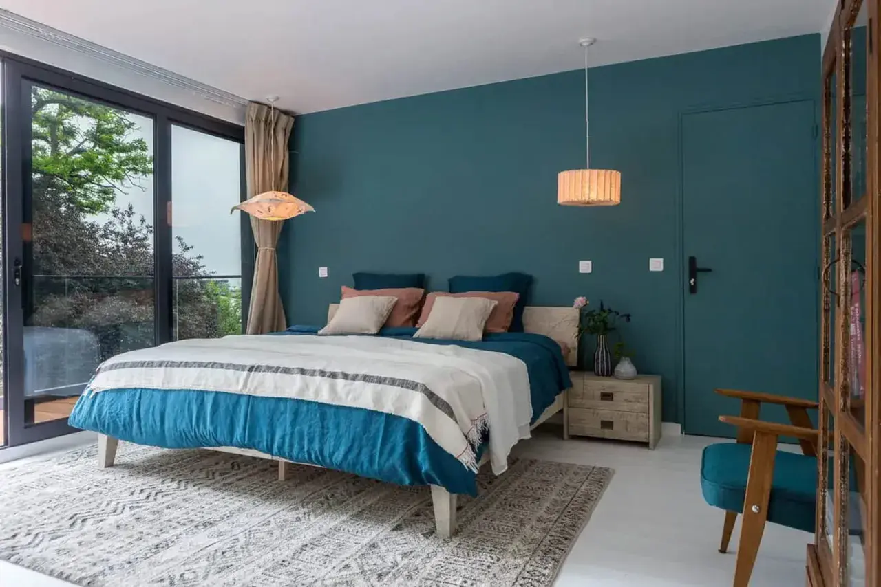 Chambre bleu nuit et bois, avec un grand lit douillet, une fenêtre donnant sur la verdure et une touche de naturel.
