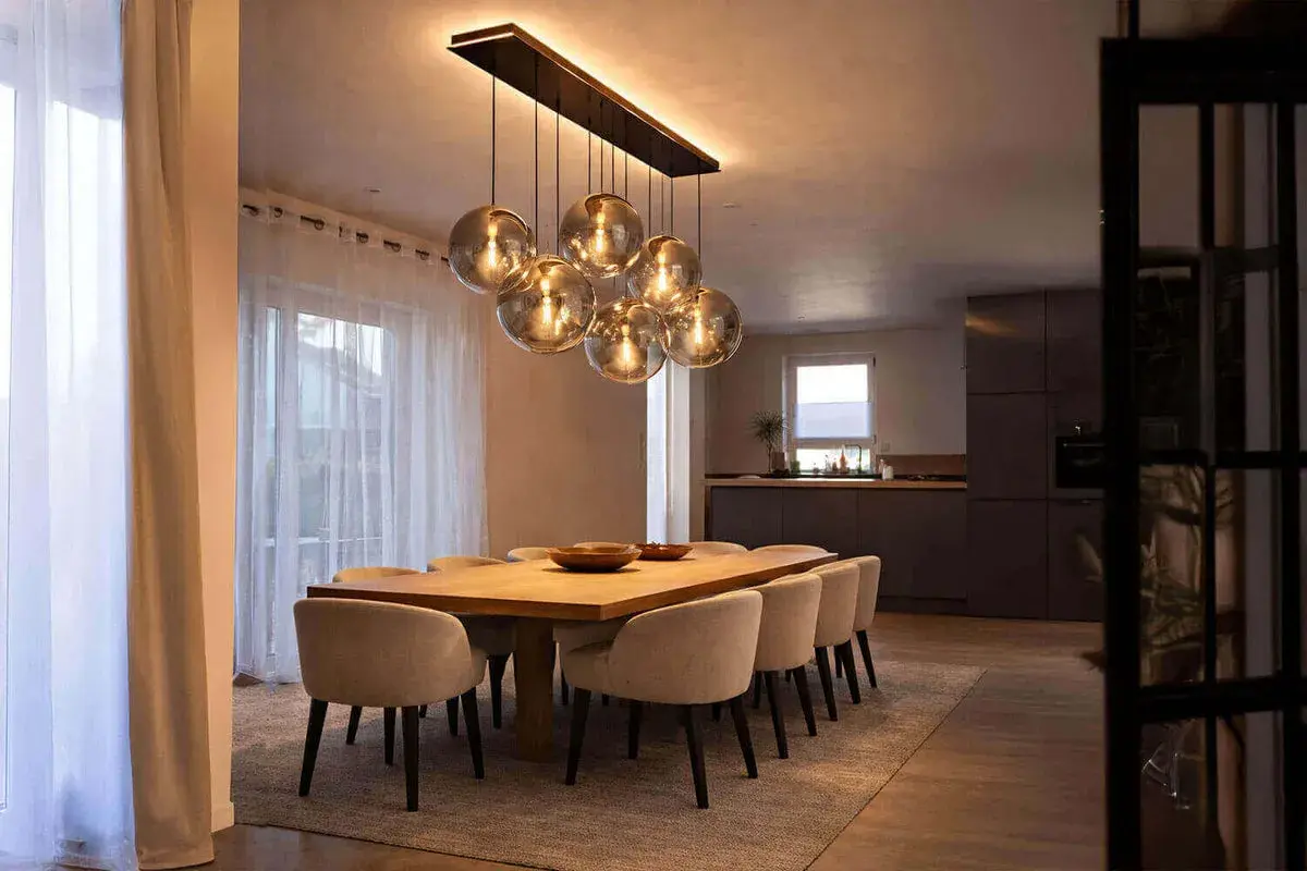 Une table à manger moderne avec des chaises confortables, éclairée par un lustre sphérique, une vraie tendance luminaire.
