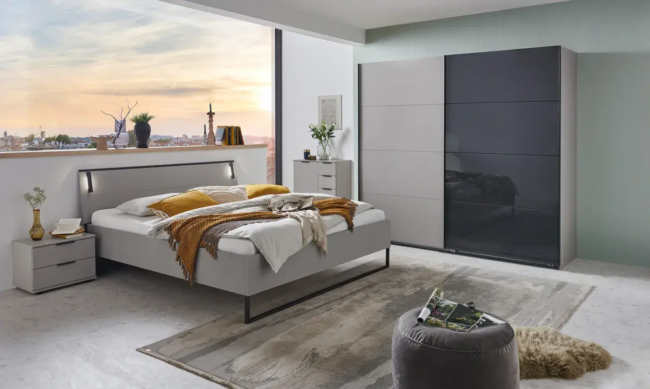 Chambre grise cocooning avec lit douillet, armoire moderne et vue sur la ville au coucher du soleil.