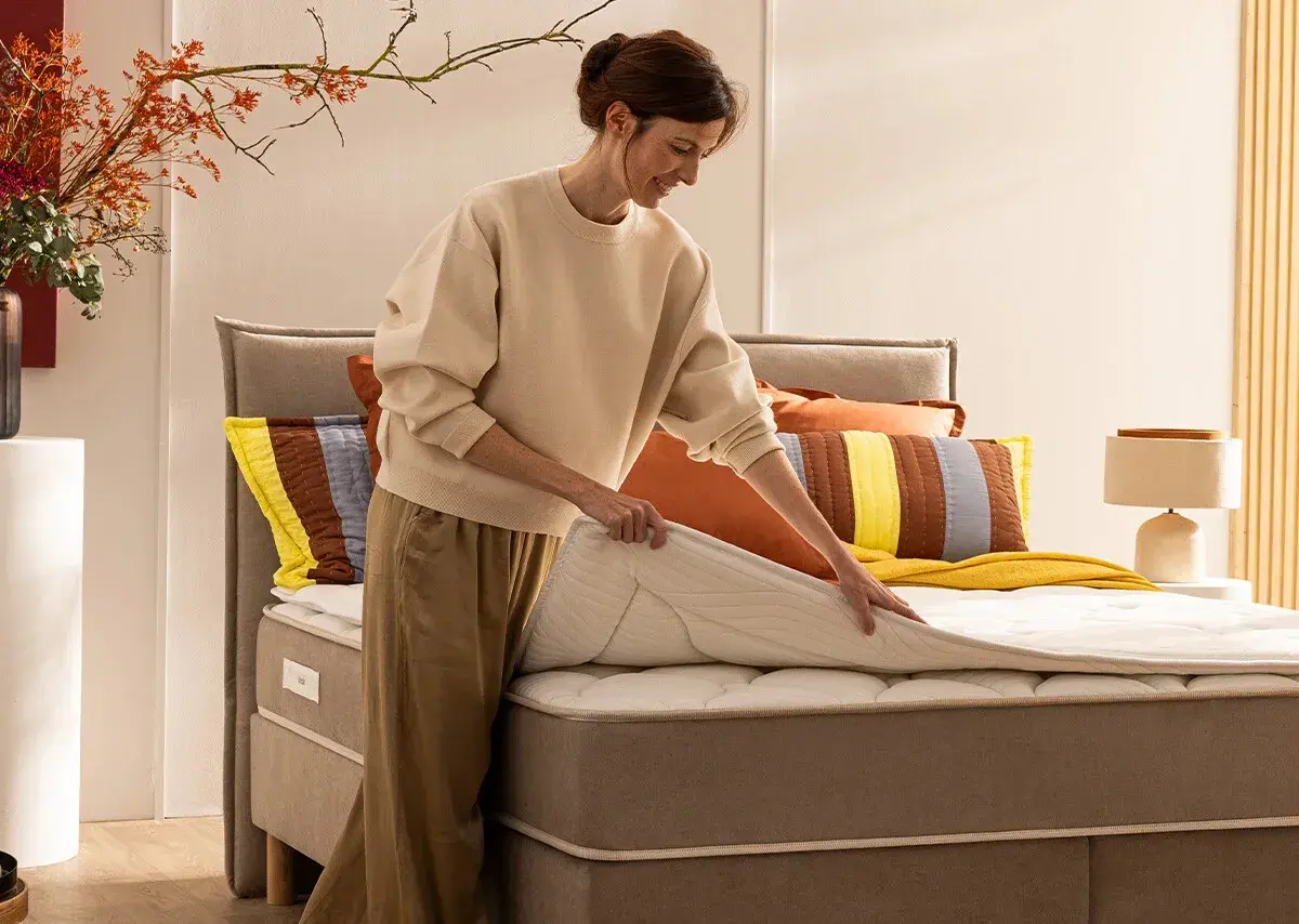 Une femme ajuste un surmatelas sur un lit. Idéal pour savoir comment surélever un lit et améliorer le confort.