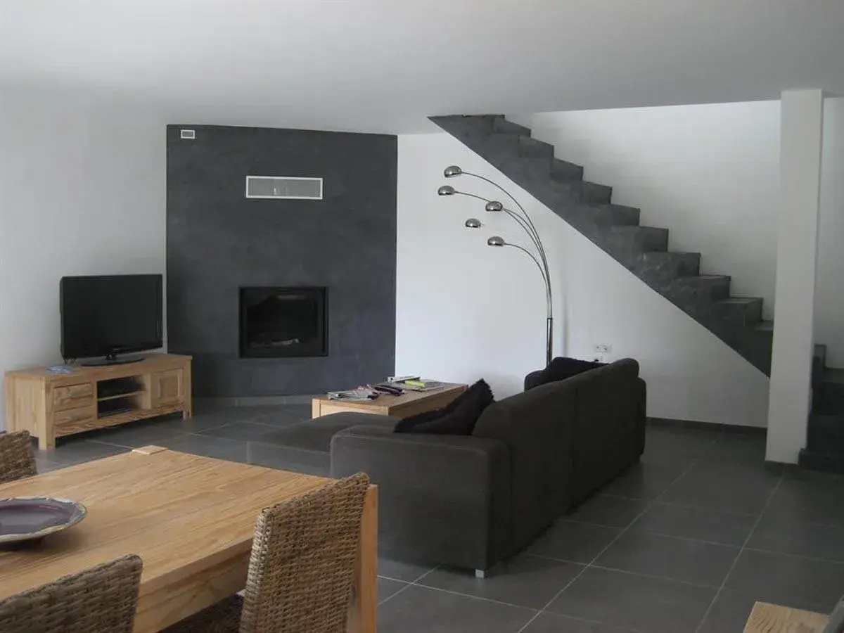 Salon moderne avec mur noir autour de la cheminée, sol gris foncé, escalier en béton, canapé marron et meuble TV en bois. Quelle couleur de mur avec un sol gris foncé ? Le noir contraste bien.