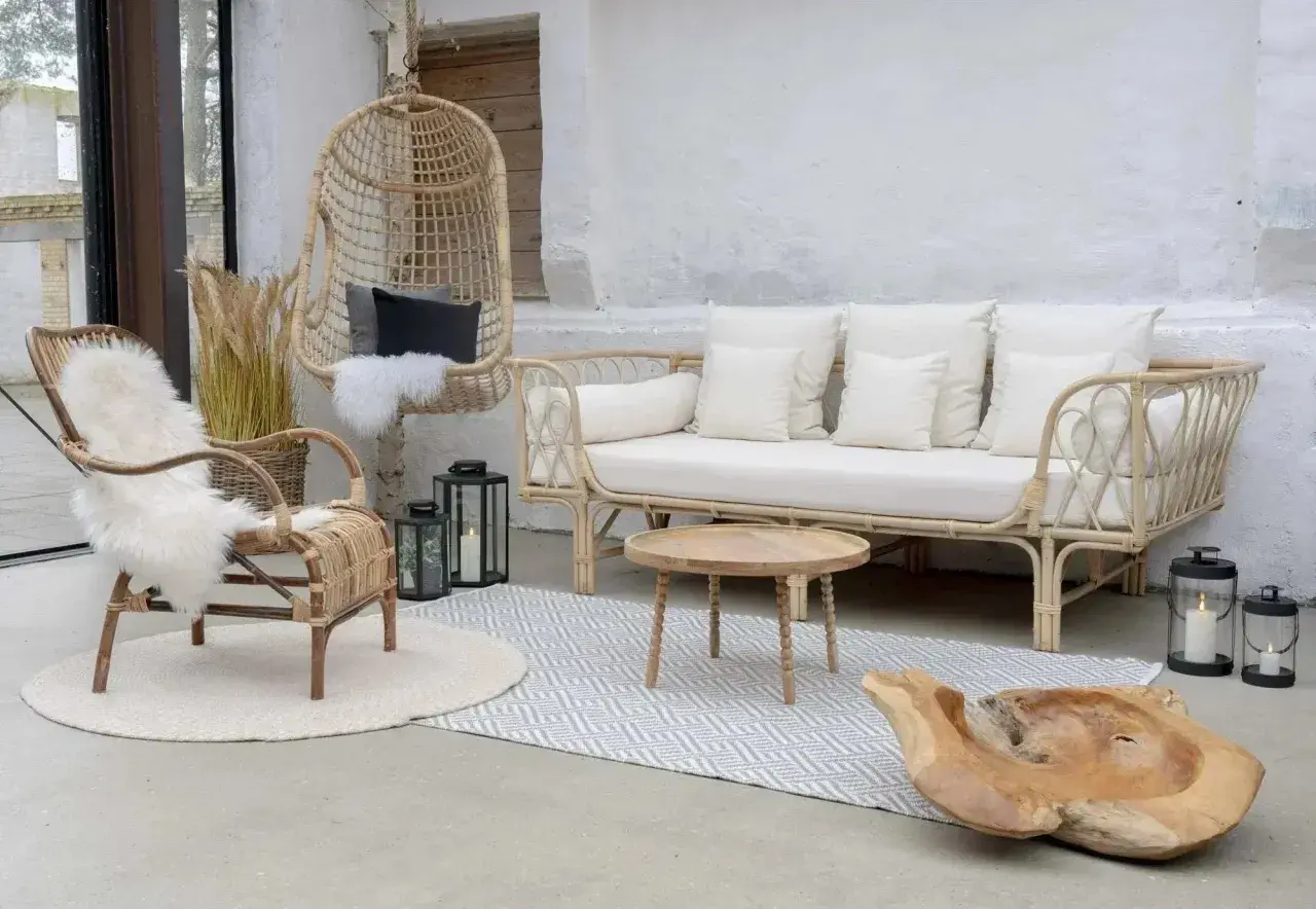 Salon avec une ambiance deco boheme chic. Fauteuil en rotin, canapé blanc, table basse en bois, et un fauteuil suspendu.