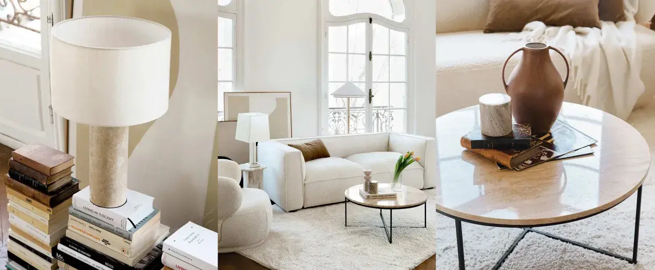 Un salon sans tv, ambiance cosy avec canapé blanc, table basse en marbre et lampes. Des livres et des vases décorent l'espace.