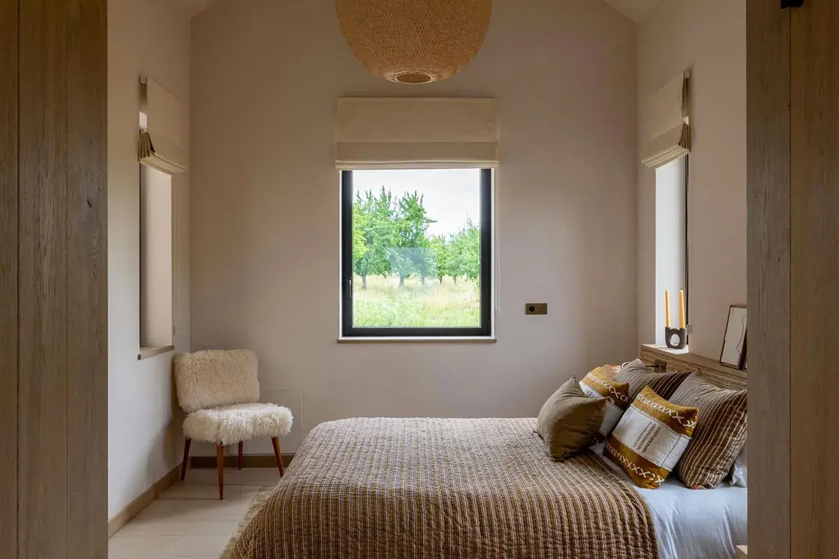 Une petite chambre parentale cosy avec un lit douillet, un fauteuil en peau de mouton et une vue sur la nature.
