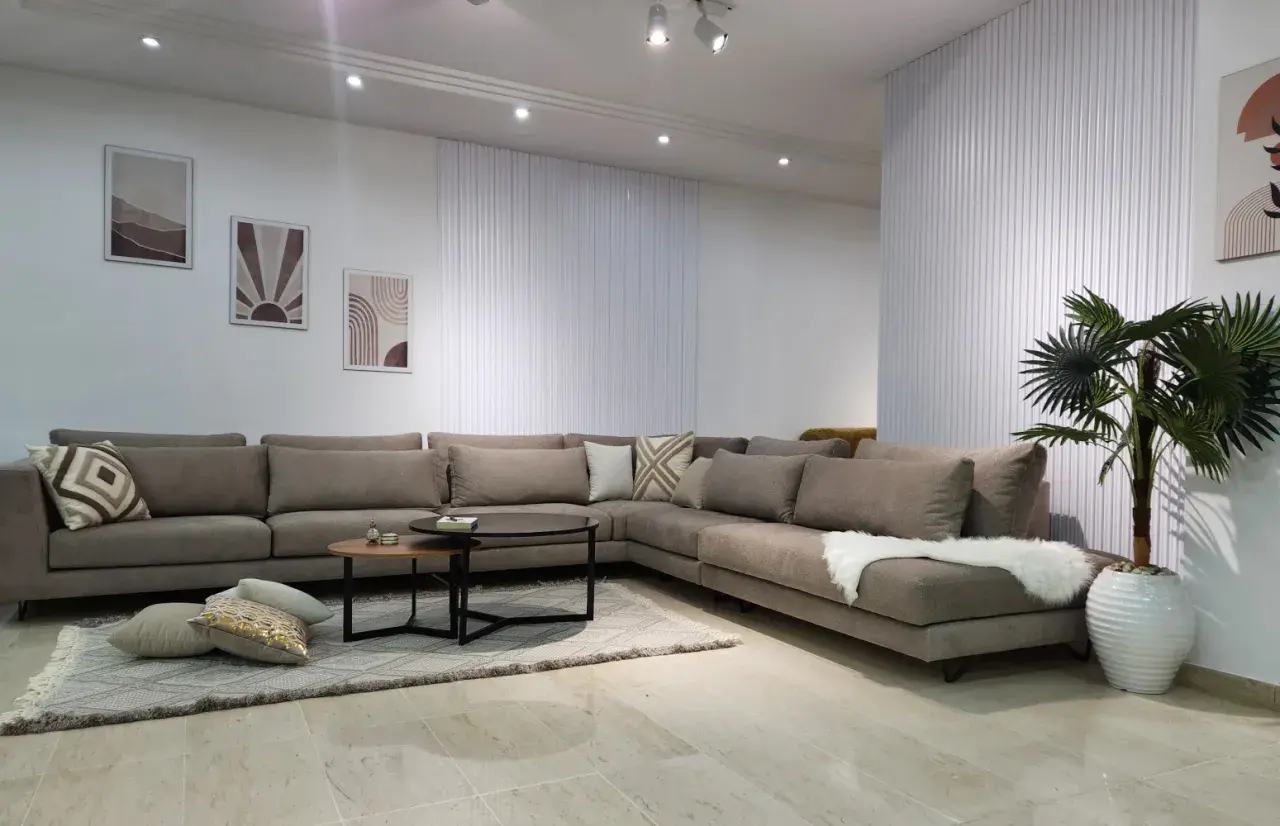 Un grand canapé d'angle taupe, parfait pour réfléchir à quelle couleur de canapé choisir. Décoration murale et plante verte complètent l'ensemble.
