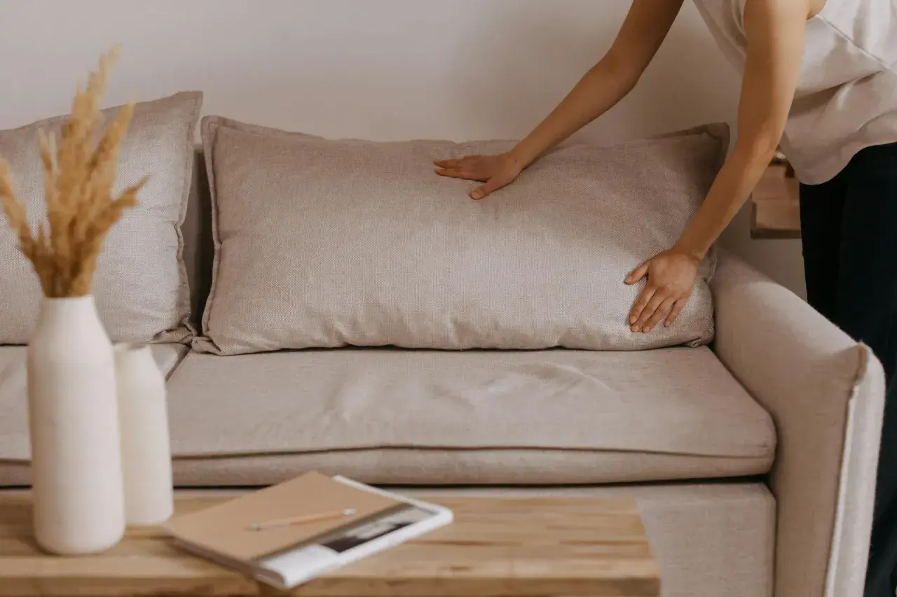 Comment faire pour le rembourrage canapé coussins avachis ? Une main ajuste un coussin pour lui redonner sa forme.