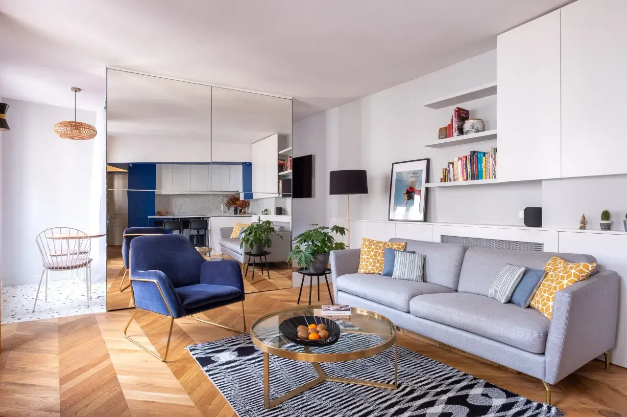 Salon moderne avec canapé gris, fauteuil bleu, table basse ronde et parquet. La deco petit appartement moderne est lumineuse et élégante.