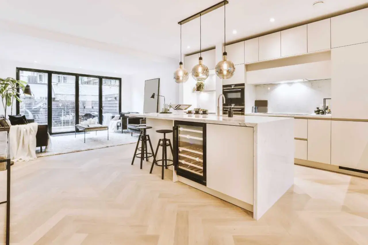 Éclairage cuisine ouverte sur salon avec îlot central, cave à vin et tabourets. Lumière douce et moderne.