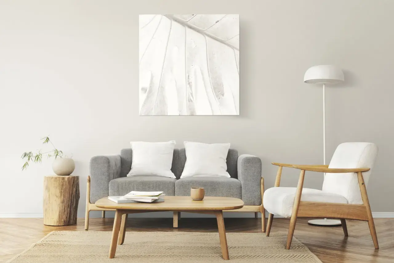Salon à la décoration minimaliste : canapé gris, fauteuil blanc, table basse en bois, tableau abstrait et lampe sur pied.