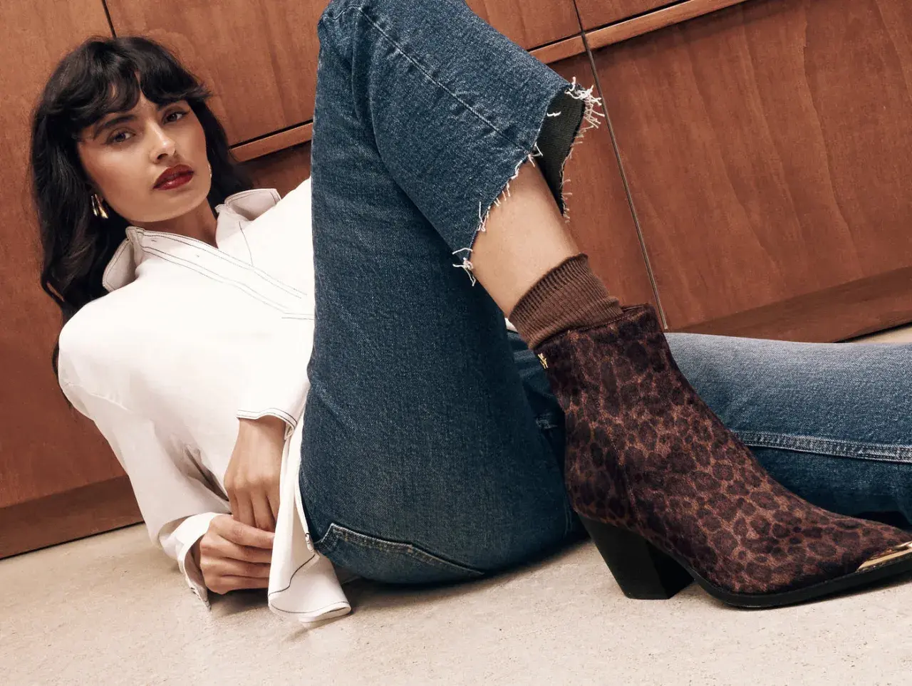 Une femme en jean et chemise blanche pose, mettant en avant sa botte au motif léopard audacieux.