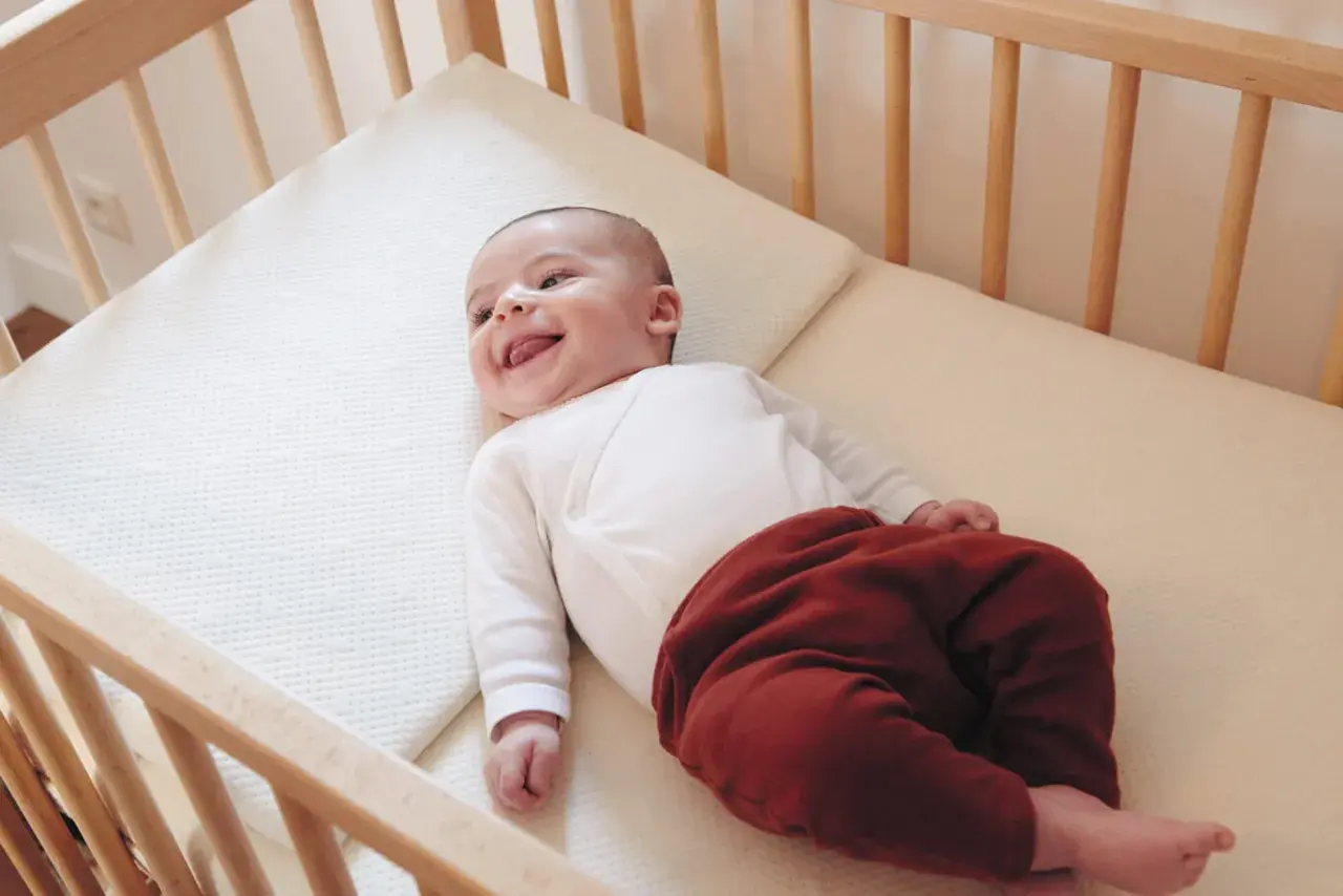 Un bébé souriant dans un lit en bois. Quel lit pour bébé est le plus confortable ? Ce matelas semble parfait pour des siestes douces.