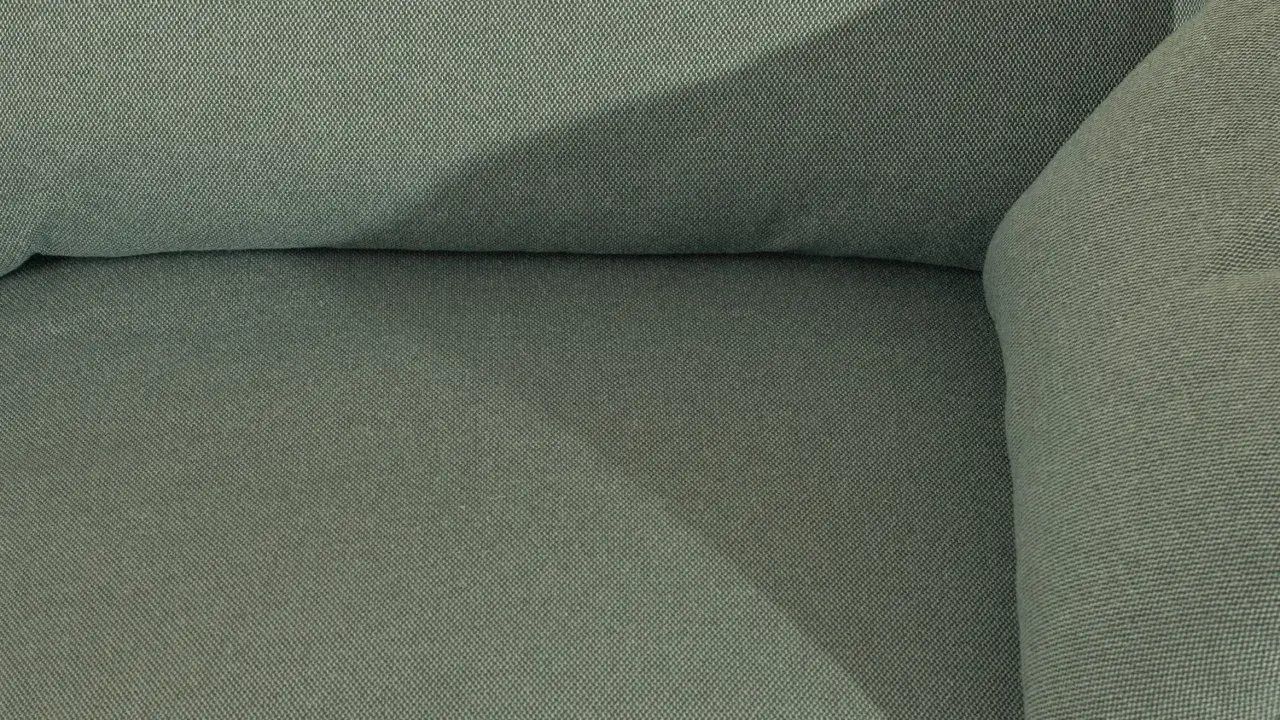 Gros plan sur le tissu texturé d'un canapé vert. Une assise de canapé qui glisse, créant une ombre douce.