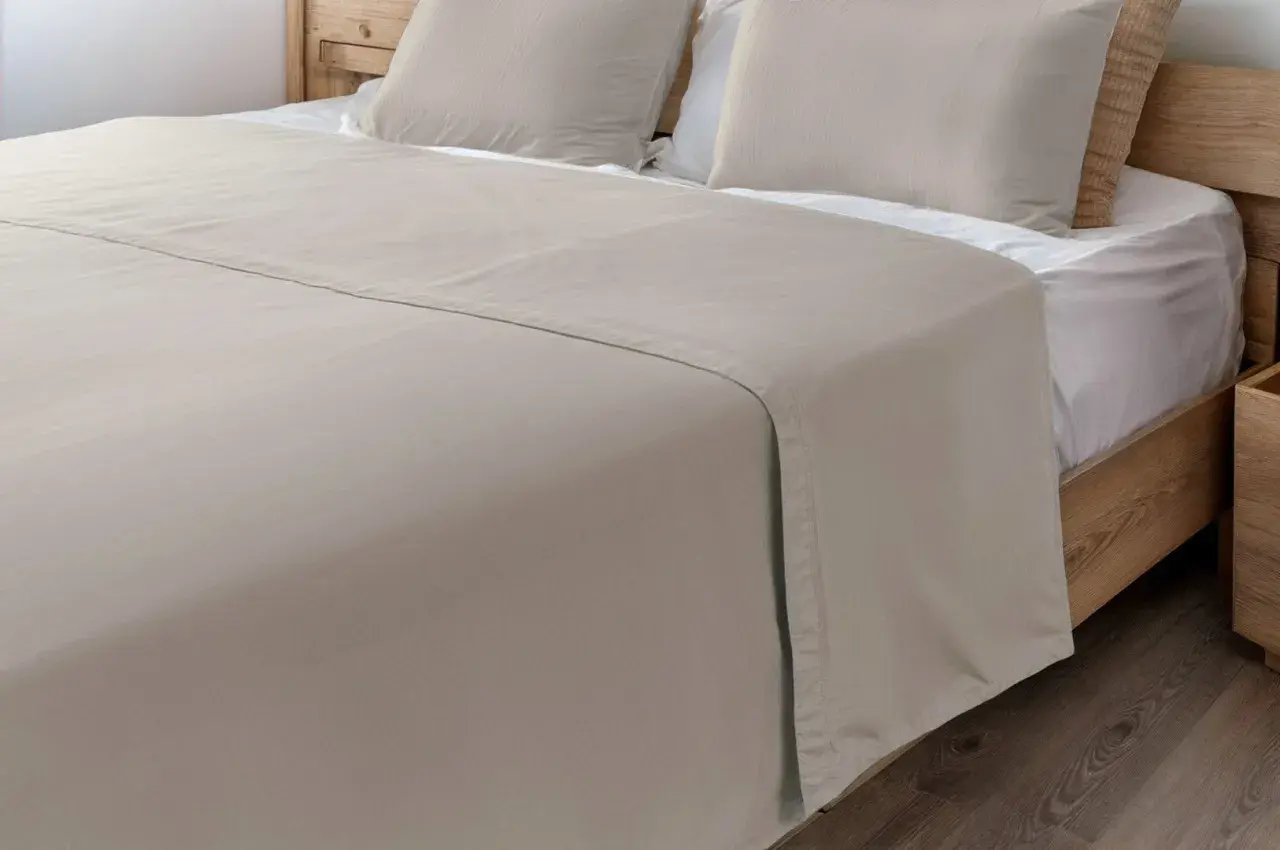 Un drap de lit beige, taille 140x190, est posé sur un lit en bois avec des oreillers assortis.