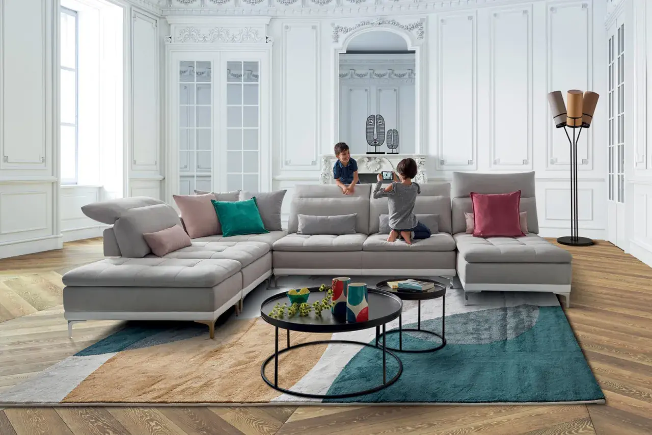 Un salon moderne et lumineux avec un canapé modulable gris, des coussins colorés et un tapis graphique. Une déco séjour tendance pour une famille.