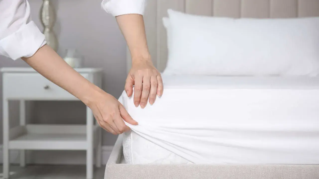 Mains ajustant un drap housse blanc sur un matelas. La question est : quelle taille de drap housse pour un lit 160x200 ?