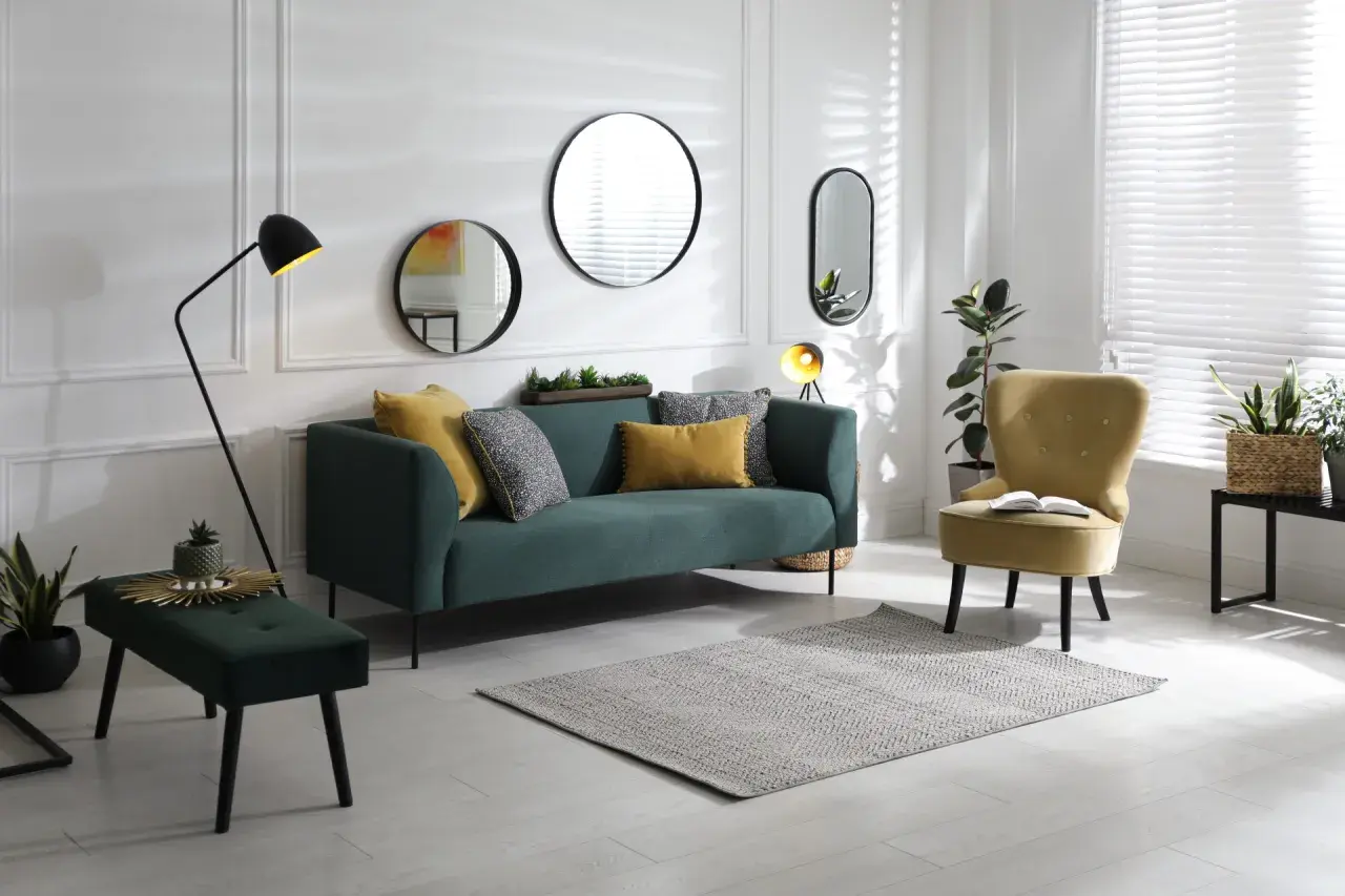Un salon moderne avec un canapé vert, un fauteuil jaune et plusieurs miroirs derrière le canapé.