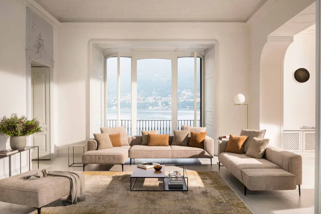 Un salon cocooning moderne avec canapé modulable, pouf, tapis et vue sur un lac.
