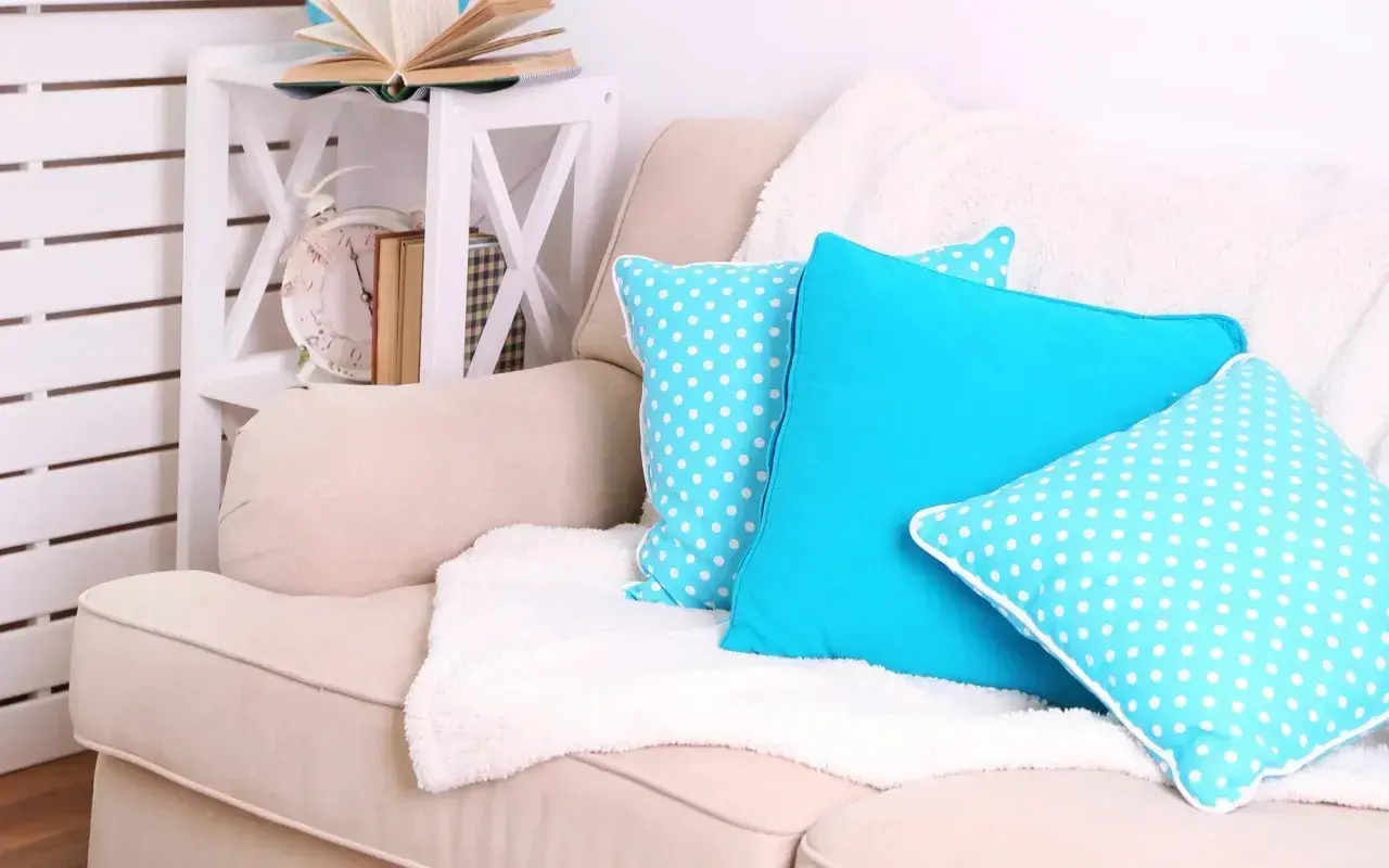 Un plaid blanc moelleux est disposé sur un canapé beige, orné de coussins bleus vifs et à pois. Idéal pour savoir comment disposer un plaid sur un canapé.
