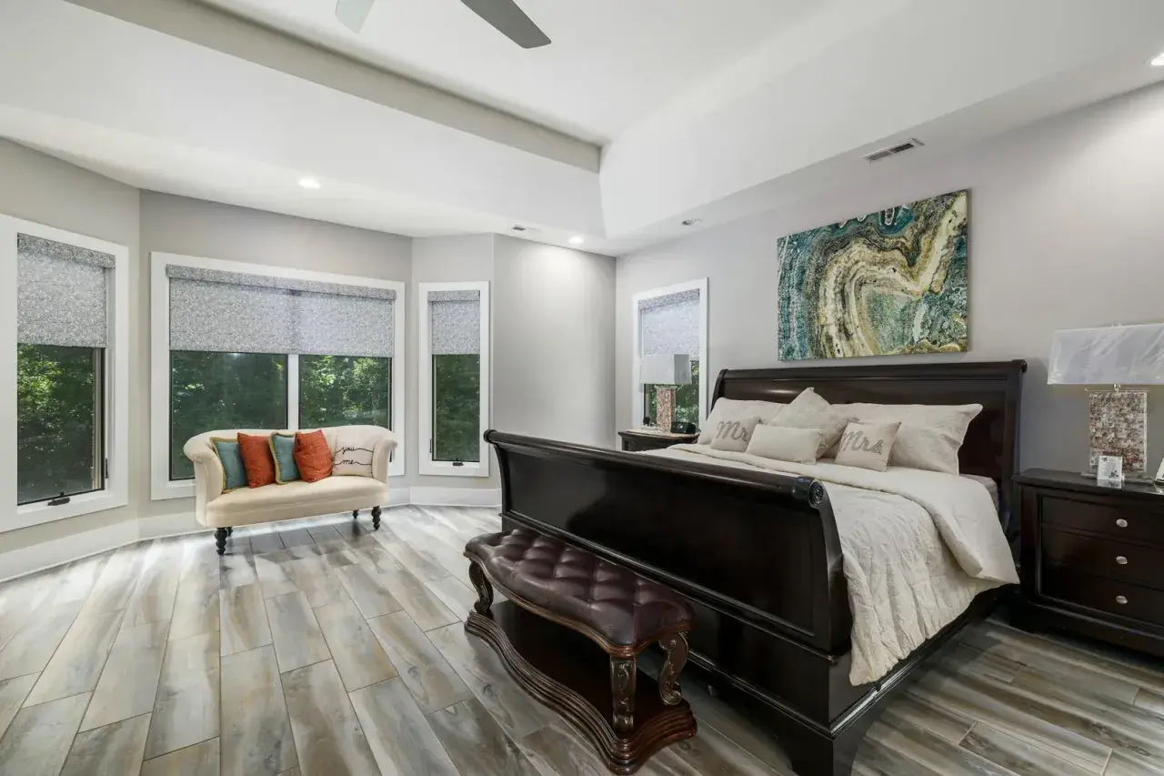 Chambre parentale spacieuse avec un grand lit, un banc en cuir, un canapé et des fenêtres donnant sur la verdure.