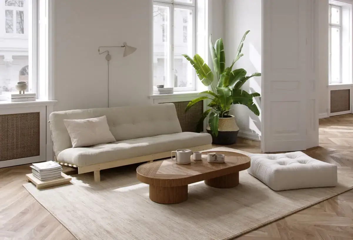 Un salon Japandi lumineux avec un canap&eacute; beige, une table basse en bois organique, une plante verte luxuriante et un pouf moelleux sur un tapis textur&eacute;.