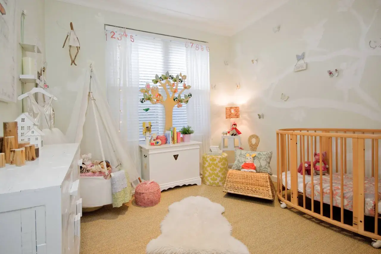Am&eacute;nagement chambre b&eacute;b&eacute; f&eacute;erique avec un berceau, un lit en bois, des jouets et une d&eacute;coration murale de f&eacute;es et d'arbres.