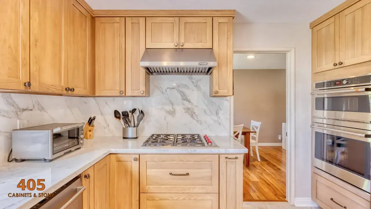 Cuisine lumineuse couleur bois clair, avec un plan de travail en marbre, une plaque de cuisson et un four.