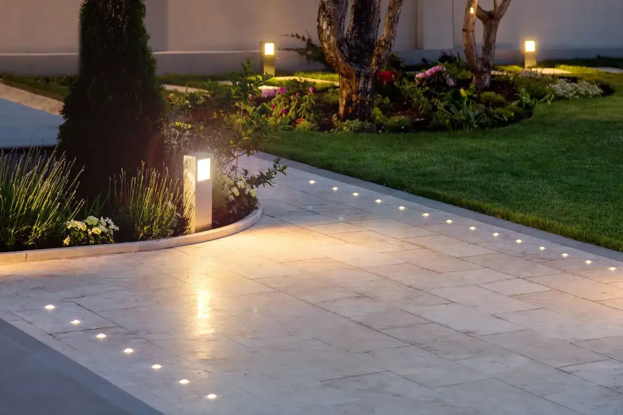 &Eacute;clairage d'all&eacute;e carrossable avec des bornes lumineuses et des spots encastr&eacute;s dans les dalles, illuminant un jardin paysager la nuit.