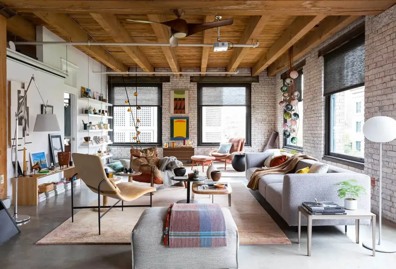 Un salon spacieux de style loft industriel avec poutres apparentes, murs en briques et mobilier confortable.