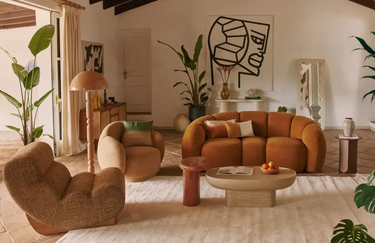 Un salon avec un canap&eacute; moche orange vif, des fauteuils textur&eacute;s, une table basse en travertin et une grande &oelig;uvre d'art abstraite.