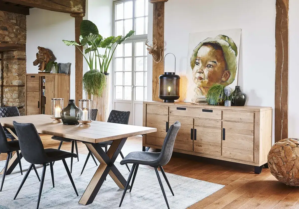 Salle &agrave; manger avec table en bois, chaises grises et buffet en ch&ecirc;ne. Une belle peinture et une plante verte apportent une touche chaleureuse &agrave; cette id&eacute;e d&eacute;co industriel.