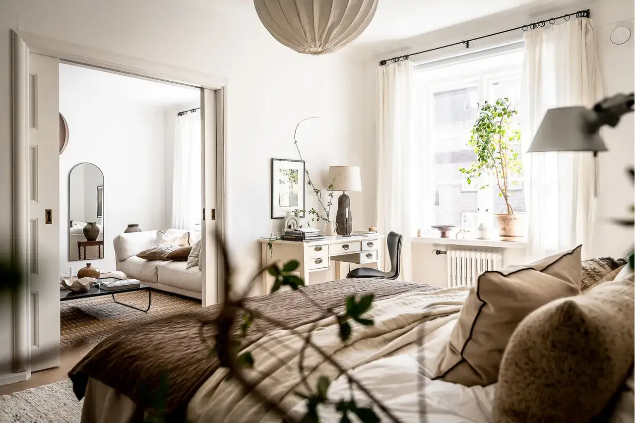 Une chambre boh&egrave;me scandinave avec un lit douillet, un bureau, et un salon invitant &agrave; travers une porte coulissante.
