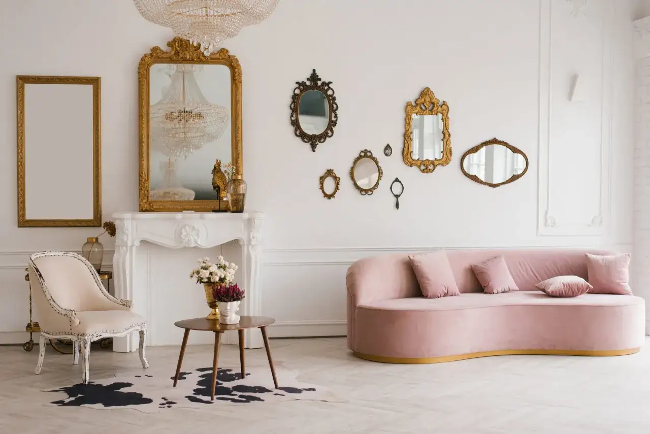 Un salon ancien moderne avec un canap&eacute; rose, une chaise vintage, une chemin&eacute;e orn&eacute;e et de nombreux miroirs dor&eacute;s.