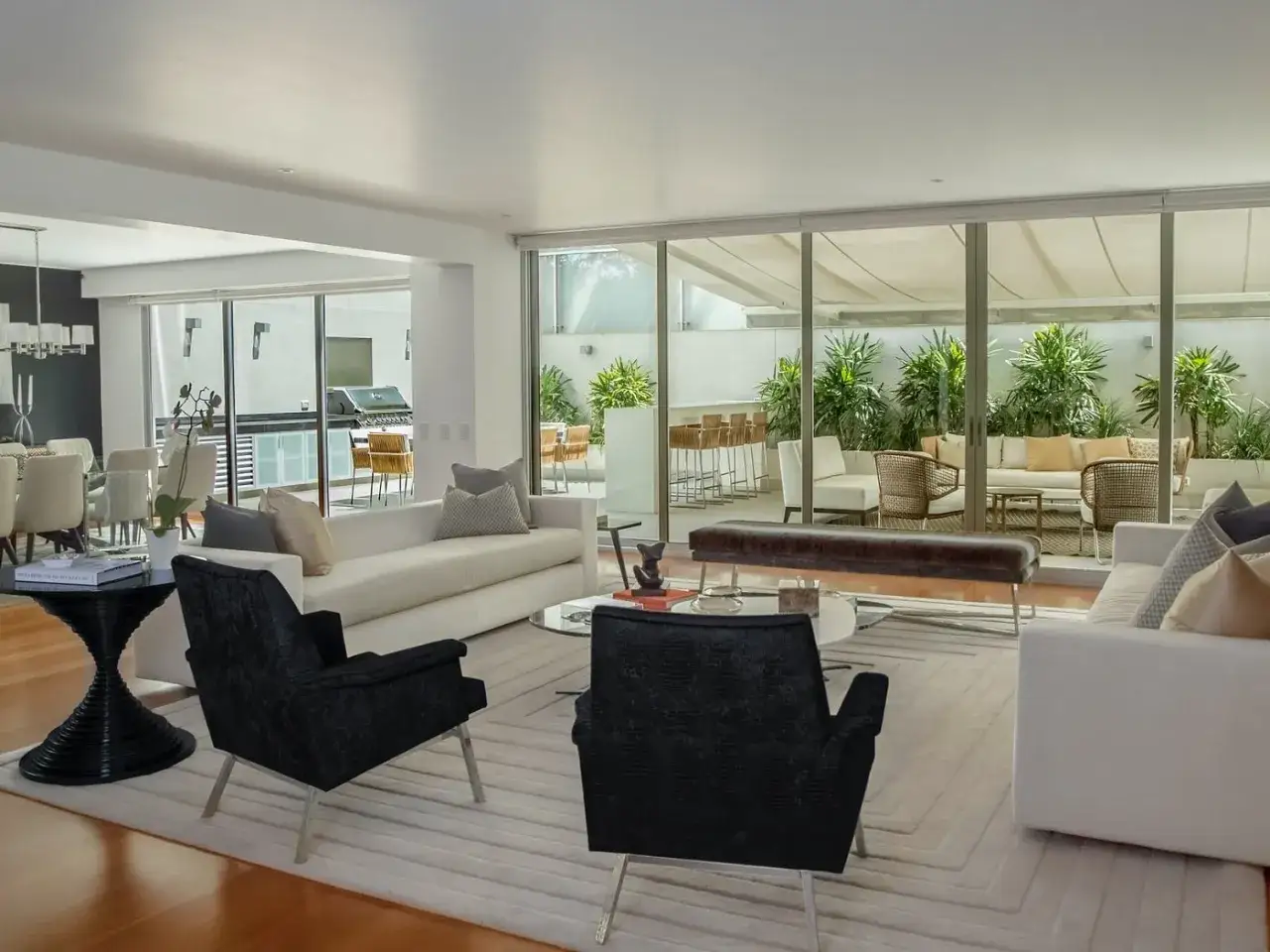 Un salon moderne avec deux canap&eacute;s face &agrave; face, des fauteuils noirs et une grande baie vitr&eacute;e donnant sur un jardin luxuriant.
