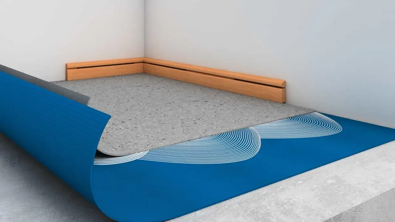 Sous un matelas au sol, une sous-couche bleue avec motifs blancs et une couche grise sont pos&eacute;es sur un b&eacute;ton brut.