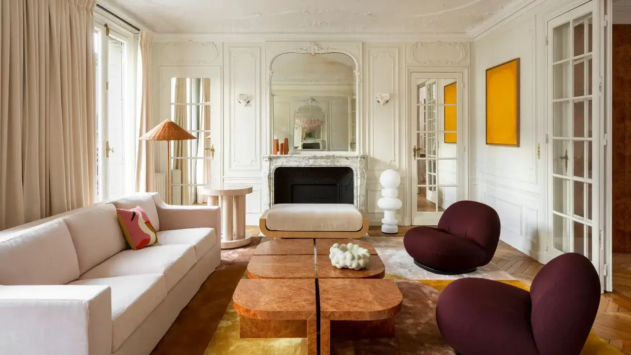 Salon chic avec canap&eacute; rose poudr&eacute;, fauteuils bordeaux, tables basses en bois et tapis abstrait. Une belle idee deco moderne.