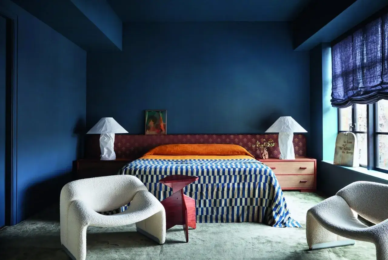 Chambre bleu nuit et bois, avec un lit aux motifs g&eacute;om&eacute;triques bleus et blancs, deux fauteuils blancs textur&eacute;s et une table de chevet en bois.