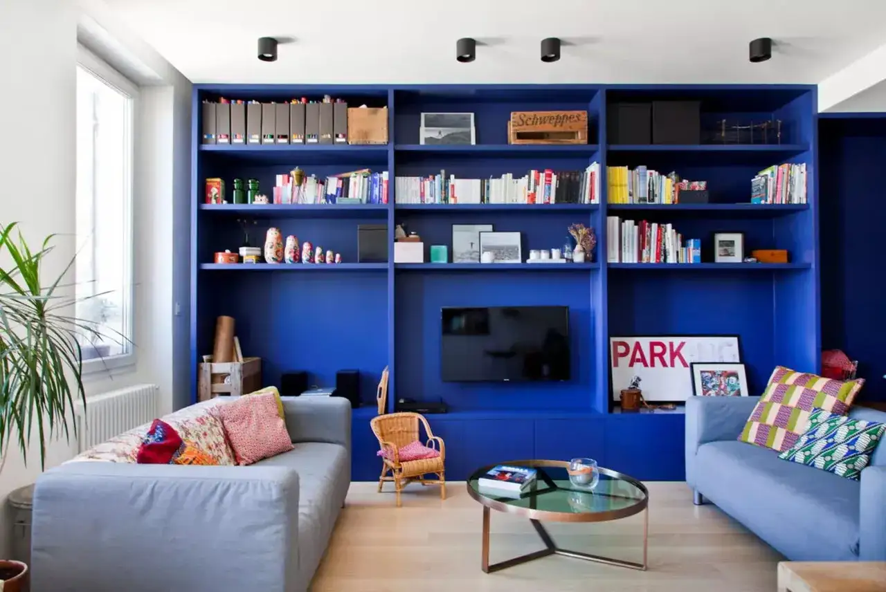 Salon moderne avec une immense biblioth&egrave;que bleu tendance, deux canap&eacute;s, une table basse et une plante verte.