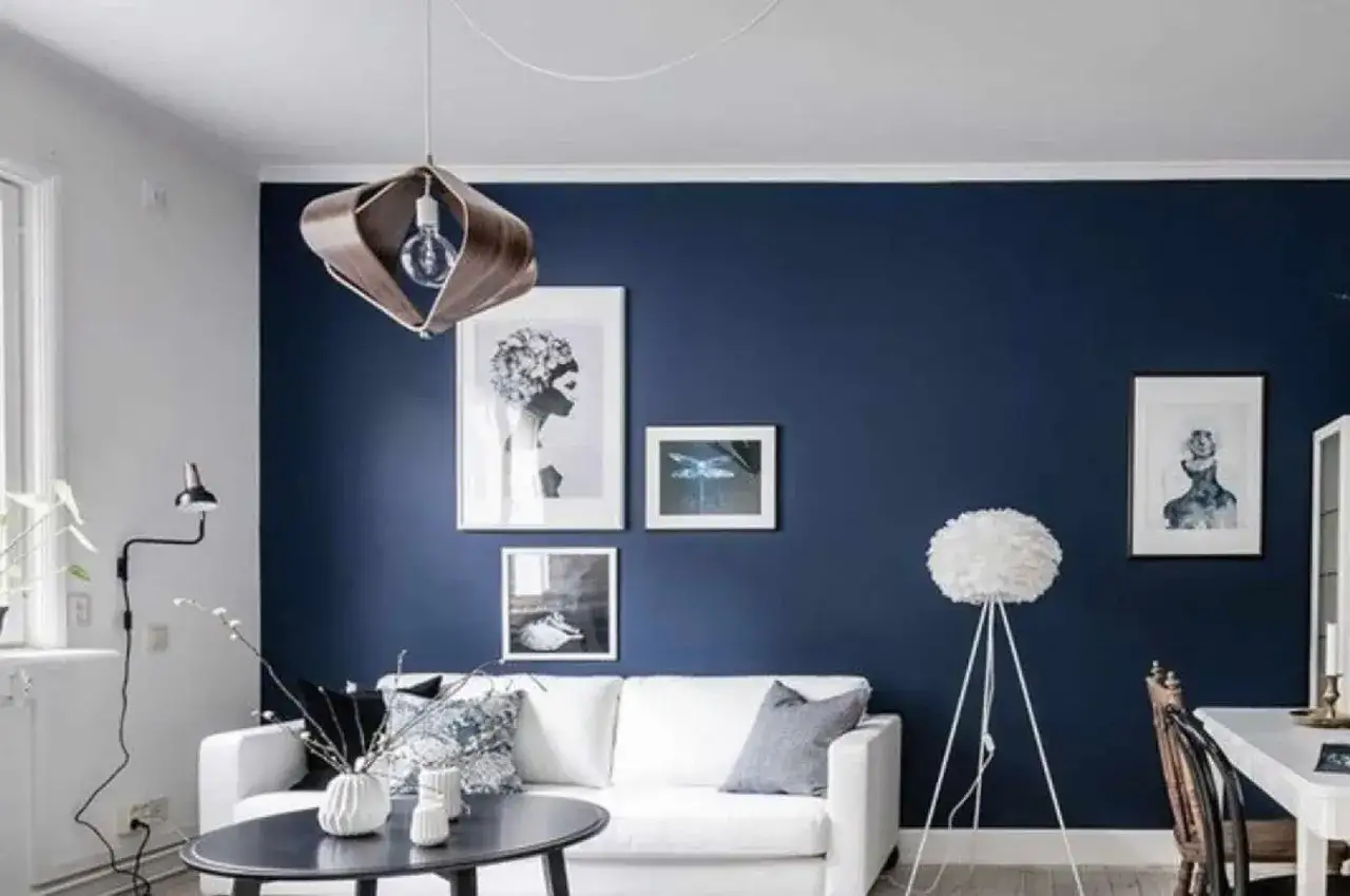 Salon moderne avec mur bleu tendance, canap&eacute; blanc, table basse ovale et plusieurs cadres d'art.