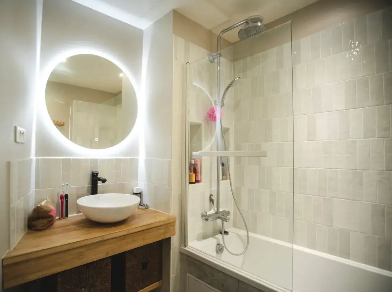 Salle de bain sombre avec vasque ronde, miroir lumineux et baignoire-douche.