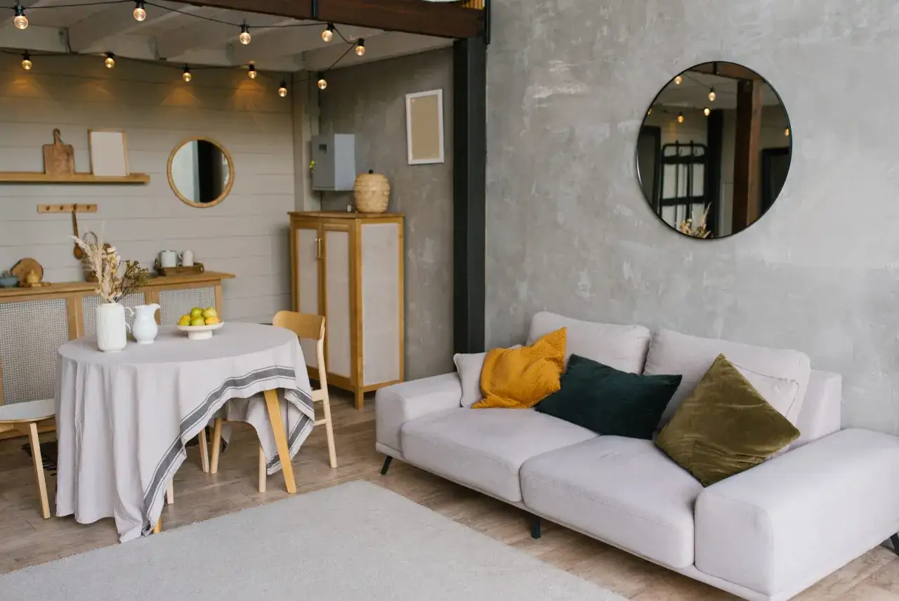 Salon moderne avec canap&eacute; clair, coussins color&eacute;s, table ronde et miroir rond. Une ambiance chaleureuse pour une deco interieur tendance.