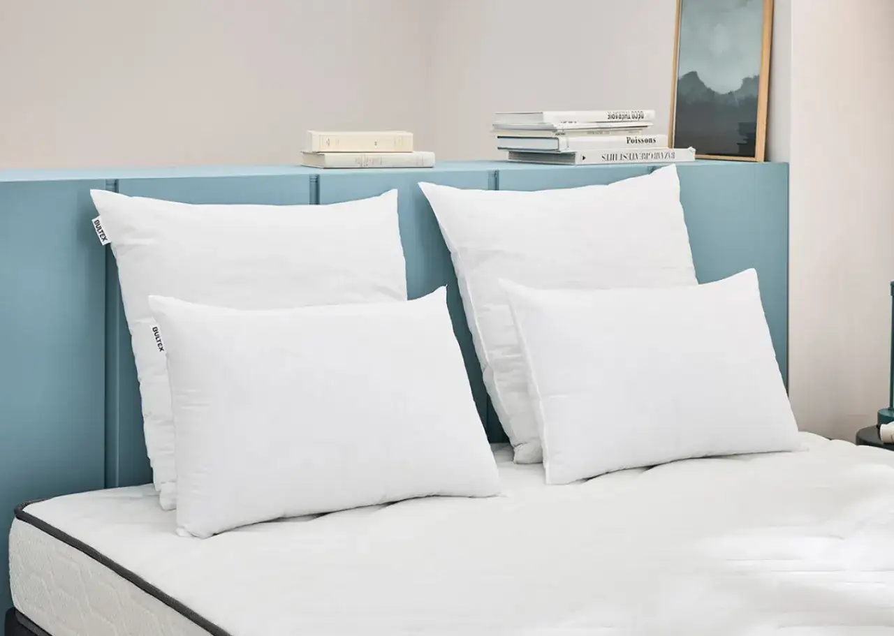 Quatre oreillers blancs, de taille oreiller standard, sont dispos&eacute;s sur un lit. Des livres et un tableau sont sur la t&ecirc;te de lit bleue.