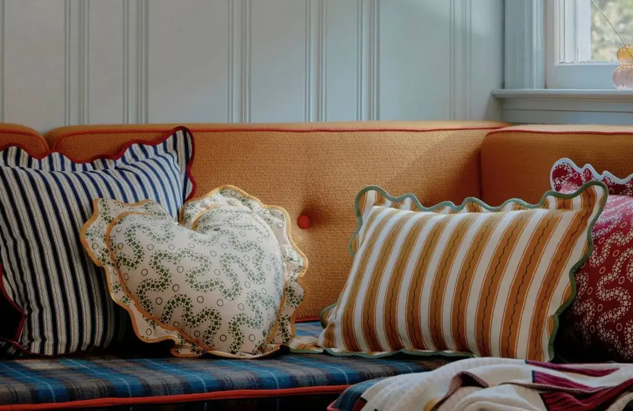 Plusieurs coussins aux motifs vari&eacute;s, dont un en forme de c&oelig;ur, d&eacute;corent un canap&eacute; orange. Le taille coussin est parfait pour un confort douillet.