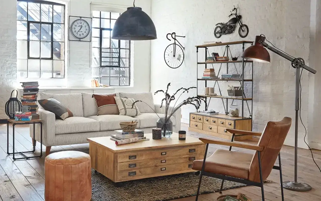 Un salon style loft avec canap&eacute; confortable, table basse en bois, fauteuil en cuir et &eacute;tag&egrave;res industrielles. D&eacute;coration murale originale avec un v&eacute;lo et une moto.