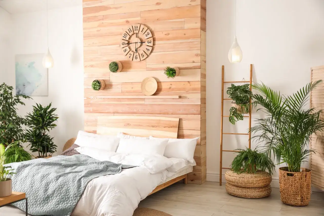 Une petite chambre cocooning avec un lit blanc, une couverture bleue, des plantes vertes et un mur en bois avec une horloge.
