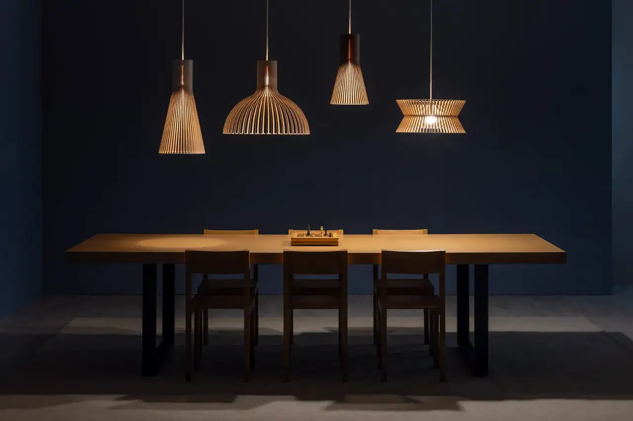 Plusieurs luminaires au dessus d'une table en bois, &eacute;clairant un jeu d'&eacute;checs pos&eacute; au centre.