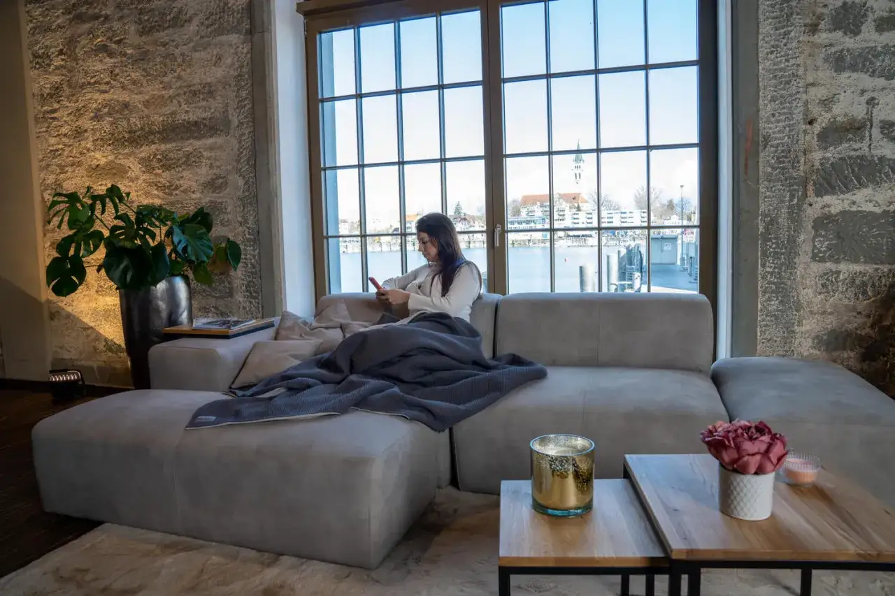 Femme en bonne position assise canap&eacute;, profitant d'un moment de d&eacute;tente avec son t&eacute;l&eacute;phone, une couverture douillette sur les genoux.