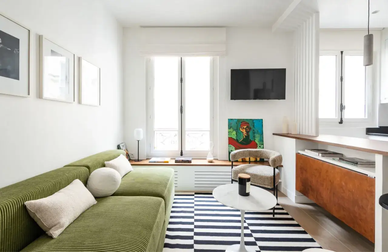 Un salon aux couleurs vives, avec un canap&eacute; vert c&ocirc;tel&eacute;, un tapis ray&eacute; et une peinture audacieuse, &eacute;voquant un style salon ann&eacute;es 70.