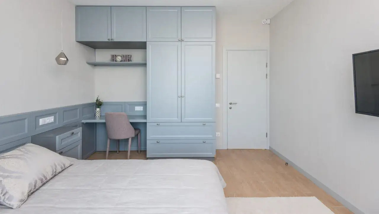 Chambre d'amis polyvalente avec lit, bureau intégré, armoire bleue et télévision murale.