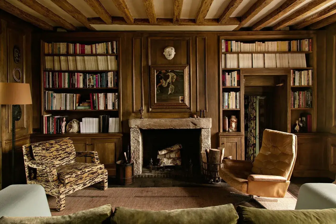 Salon au style rustique chic avec chemin&eacute;e en pierre, fauteuils imprim&eacute; animal et cuir, et biblioth&egrave;ques en bois remplies de livres.